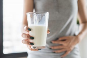 Egy pohár tejet kezében tartó, hasfájással küzdő nő, mely a laktáz enzim hiányának egyik tünete