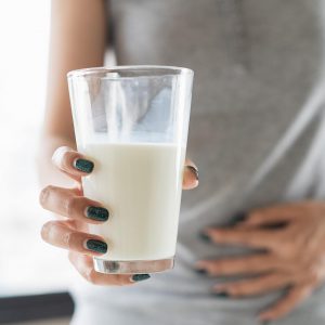 Egy pohár tejet kezében tartó, hasfájással küzdő nő, mely a laktáz enzim hiányának egyik tünete